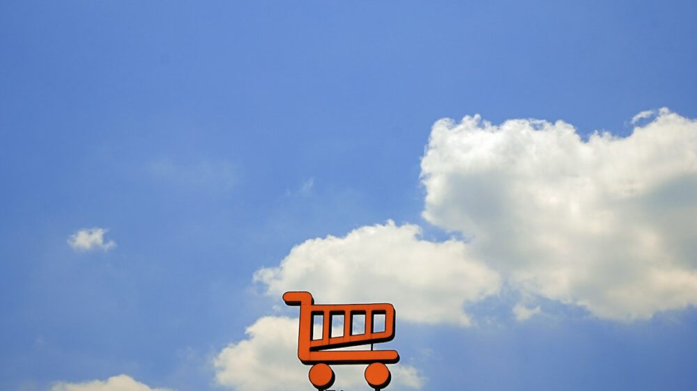 Orange shopping cart sign against a blue sky.